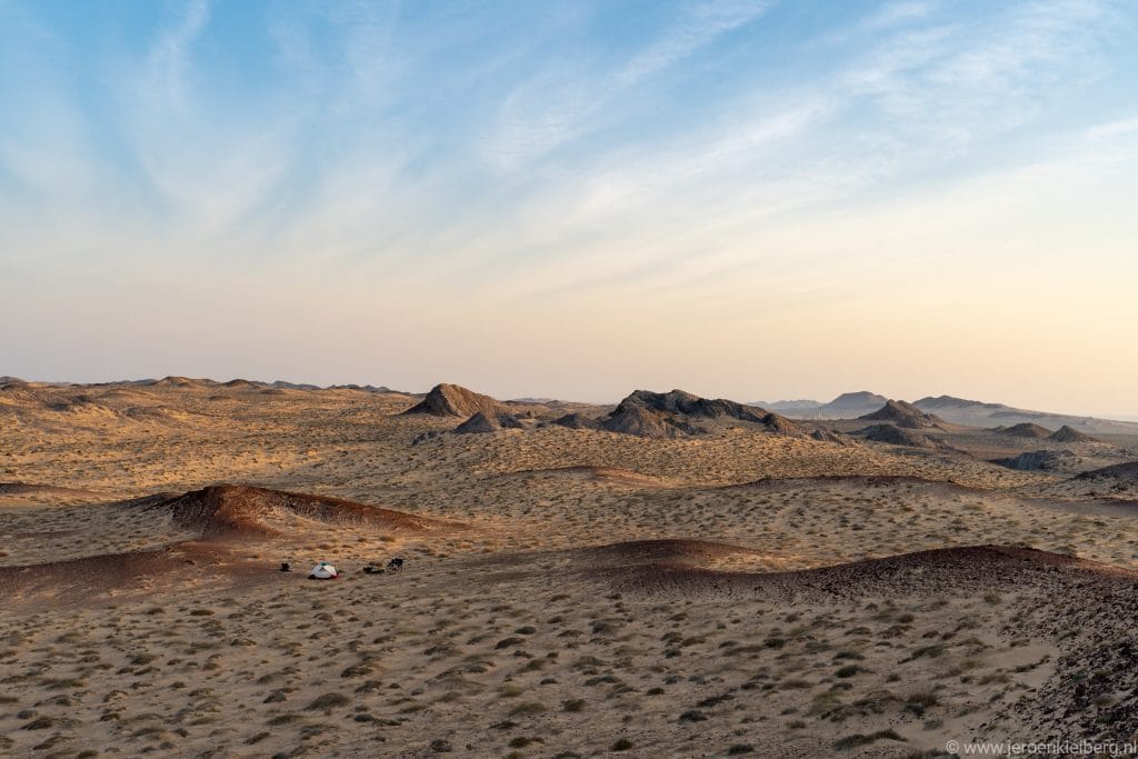 Eenzaam tentje bij lage rotskopjes in een uitgestrekte woestijnvlakte in Oman bij ochtendgloren