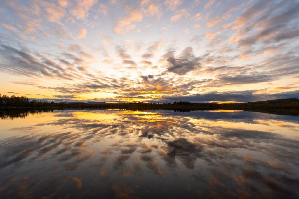 Oranje zonsondergang boven een spiegelglad meer nabij Kiruna in Zweeds Lapland met dramatische wolkenlucht