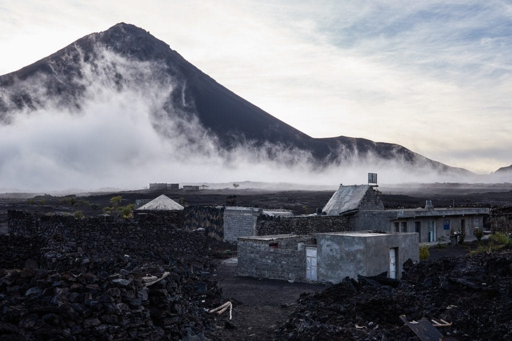 Pico do Fogo-vulkaan omhuld door wolken boven het zwarte lavadorp Chã das Caldeiras op Fogo, Kaapverdië