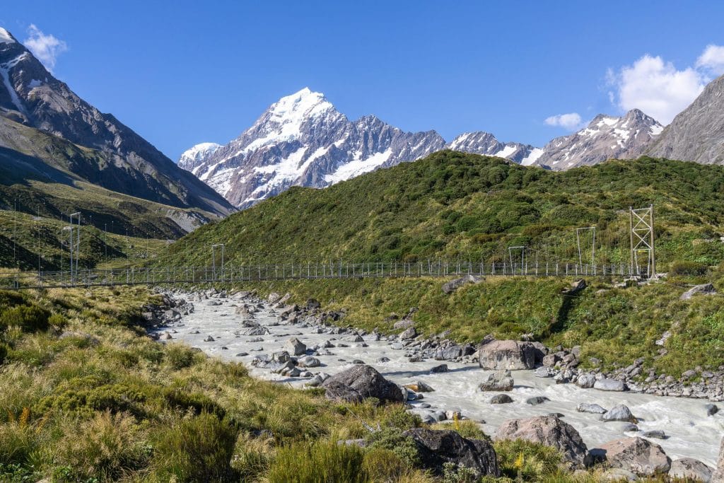 Aoraki/Mount Cook met besneeuwde toppen boven een vallei met hangbrug en gletsjierrivier in het Mount Cook Nationaal Park