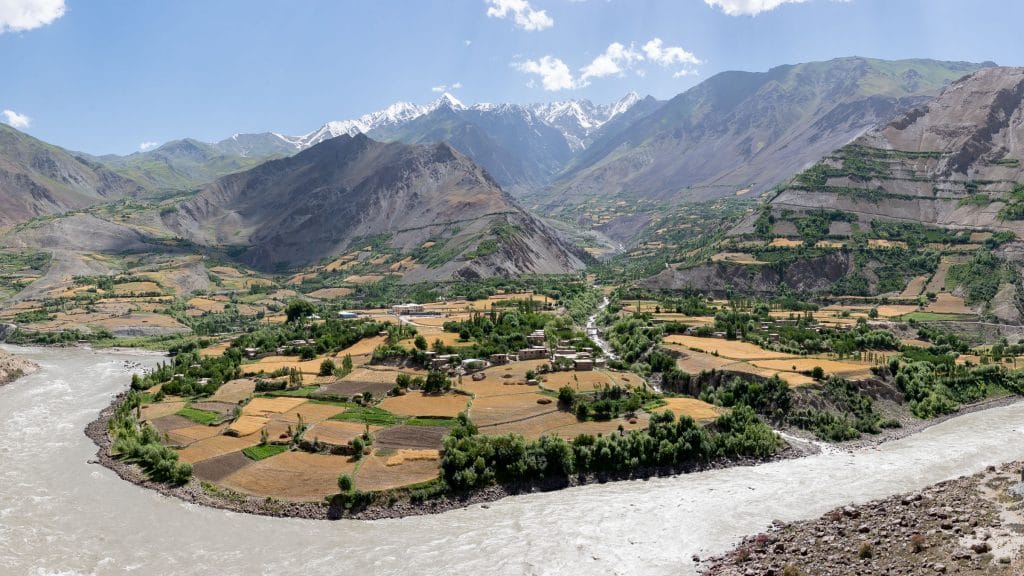 Uitzicht over de Afghaanse Wakhancorridor met groene valleivelden, een rivier en besneeuwde bergtoppen, gezien vanuit Tadzjikistan