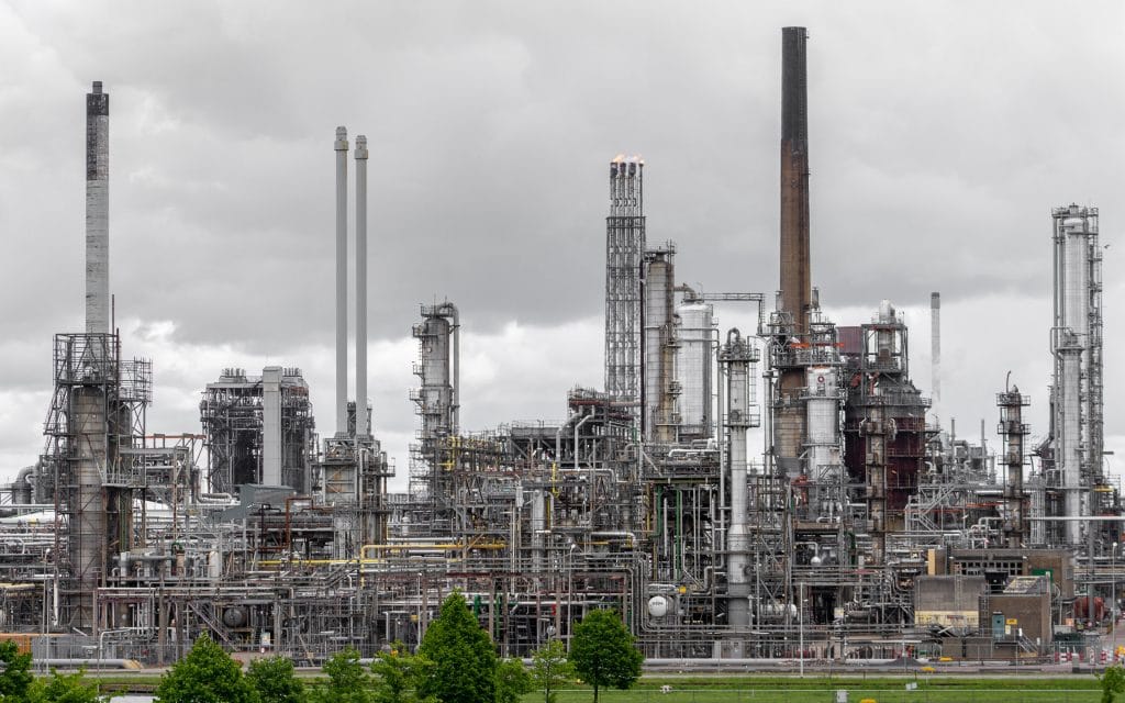 Industrieel complex met pijpen en schoorstenen van een petrochemische raffinaderij in de Rotterdamse haven onder bewolkte lucht