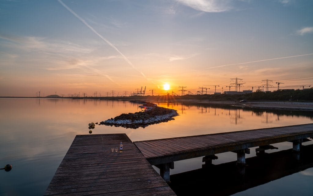 Gouden zonsondergang bij een houten steiger bij Oostvoorne in Zuid-Holland, met haveninstallaties en windmolens silhouet op de horizon