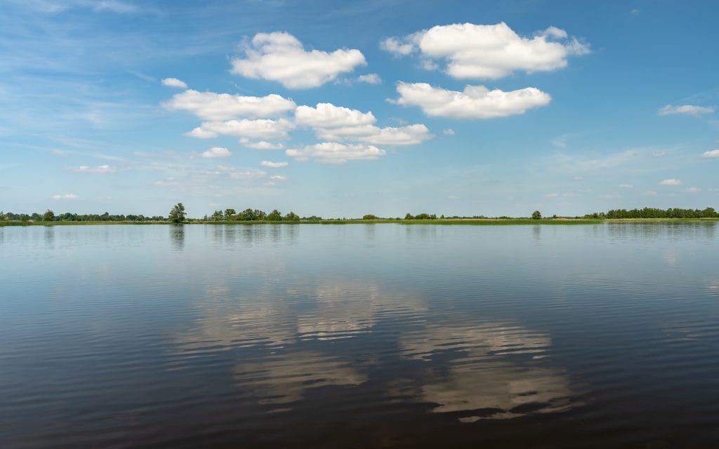 Wijds open polderwater bij Wanneperveen in Overijssel met blauwe lucht en witte stapelwolken die weerspiegelen in het water