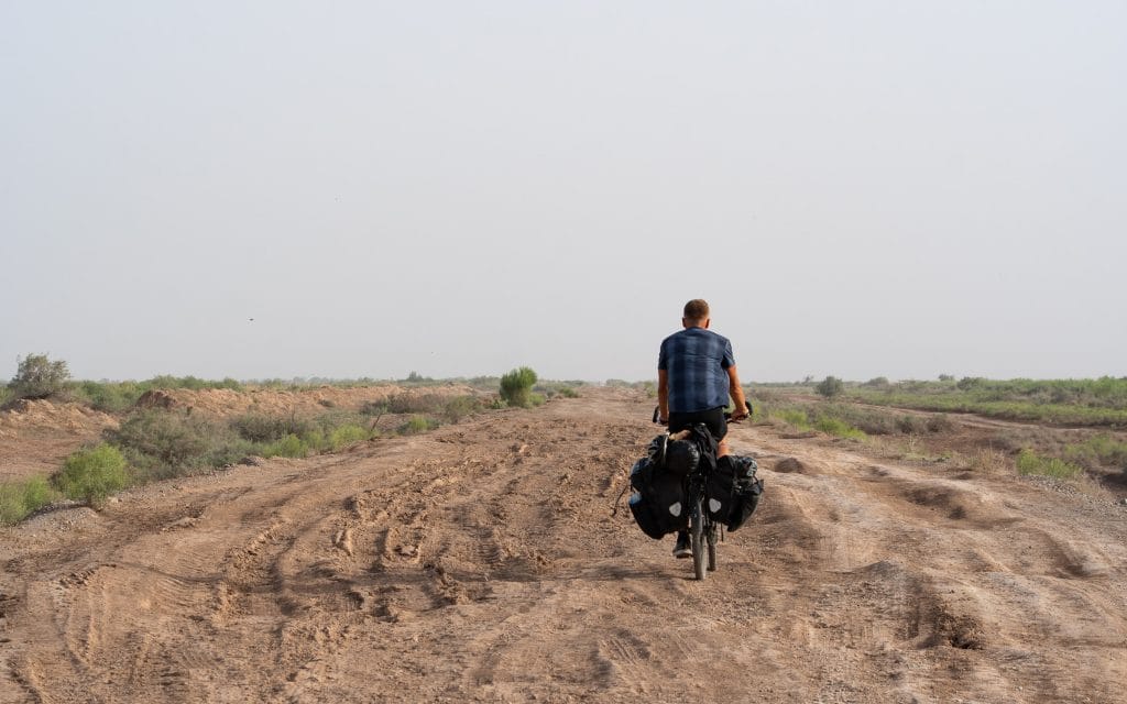 Fietser op een hobbelig zandpad door dorre steppe met lage struiken in de omgeving van Mary, Turkmenistan