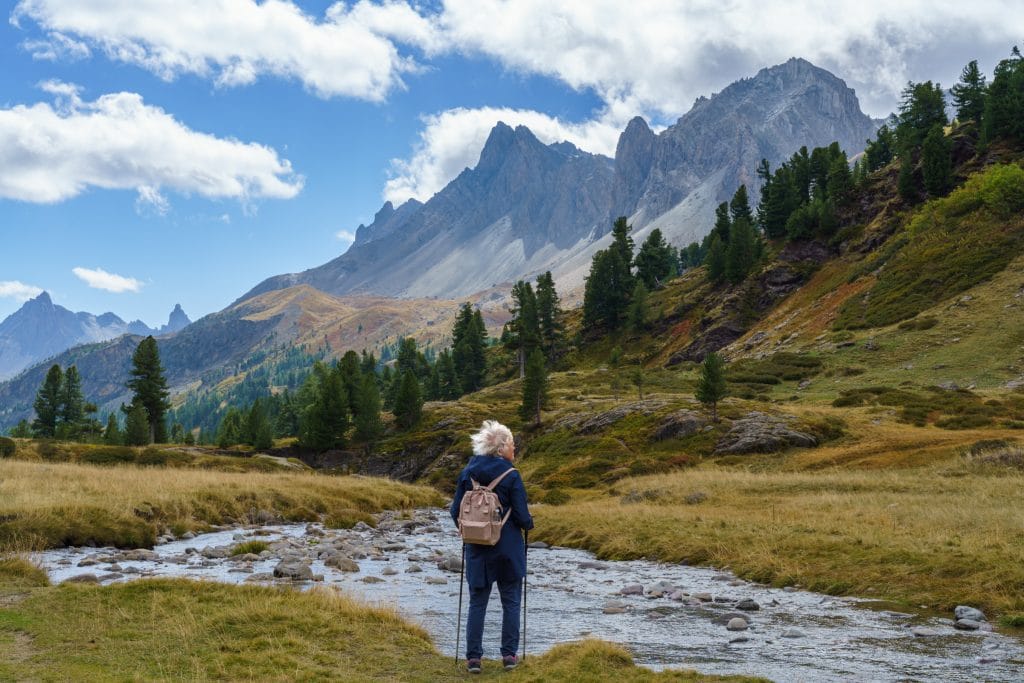 Vrouw met rugzak wandelt door een alpenweiland in de Franse Alpen richting markante spitse rotstoppen