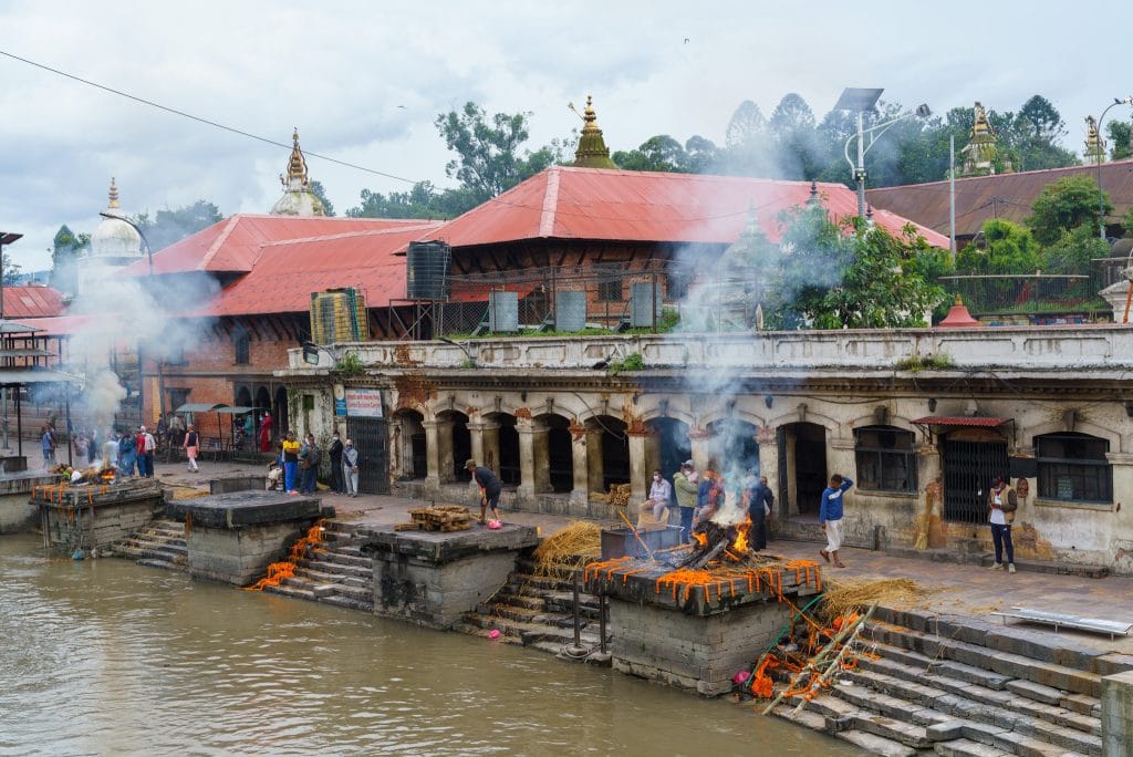 Crematieplein bij de Pashupatinath Tempel in Kathmandu met brandende crematiepyren en bezoekers langs de Bagmati-rivier