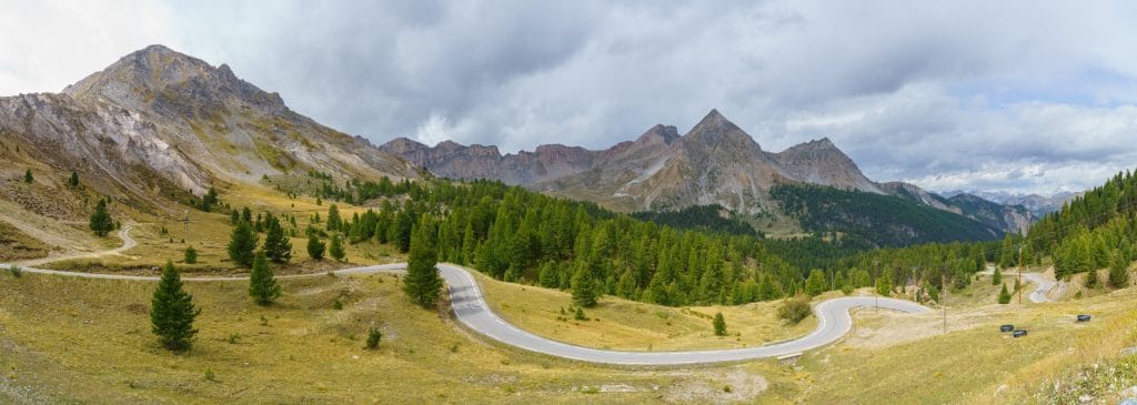 Kronkelende bergweg door naaldwoud in de Franse Alpen met kleurrijke roodachtige rotsige bergtoppen op de achtergrond