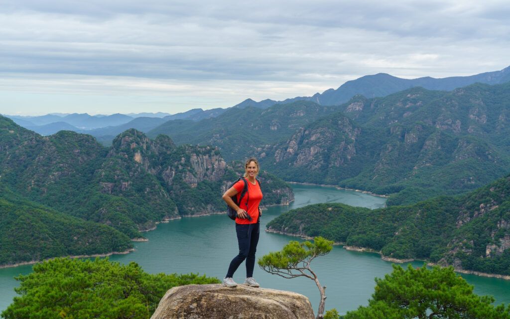 Een wandelaar poseert op een rots met een panoramisch uitzicht op de groene heuvels en kronkelende rivier in een nationaal park in Zuid-Korea.