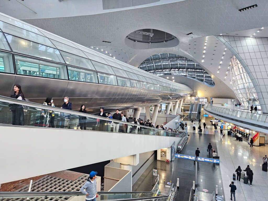 Modern interieur van Incheon International Airport met glazen wanden en reizigers op roltrappen.