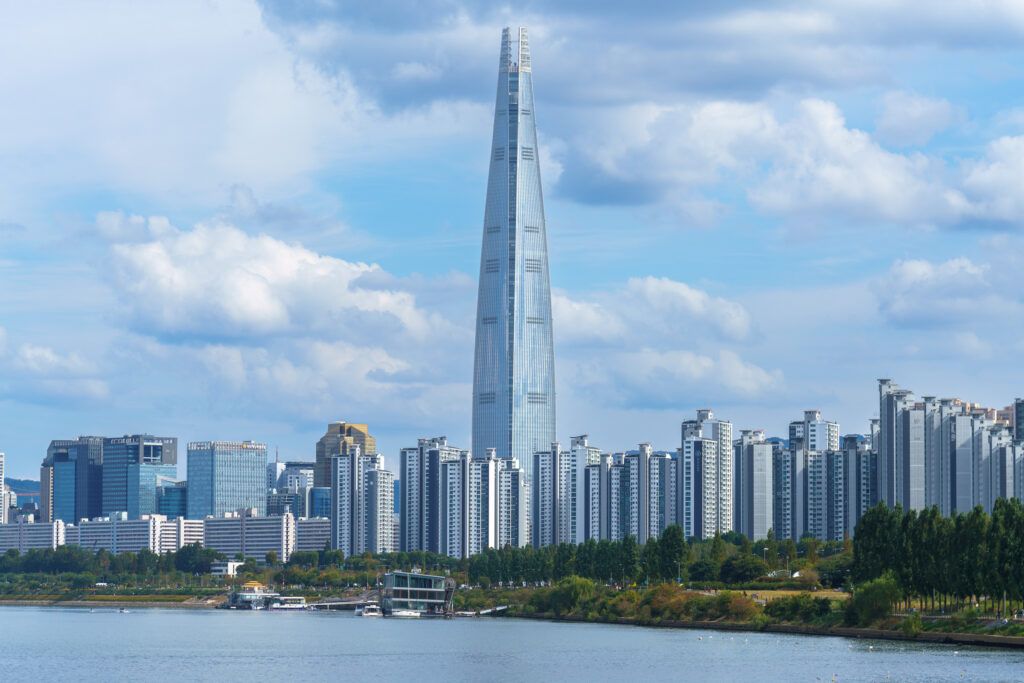 De Lotte World Tower met omliggende hoogbouw aan de rivier in Seoul onder een blauwe lucht.