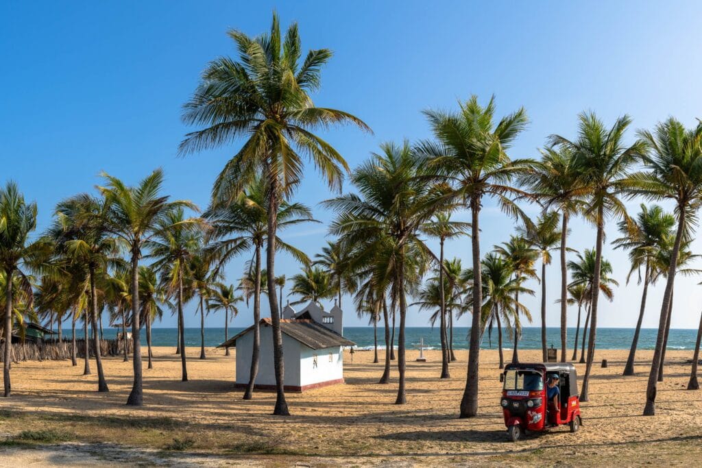 Rode tuktuk geparkeerd op een tropisch zandstrand omringd door hoge palmbomen, Sri Lanka.