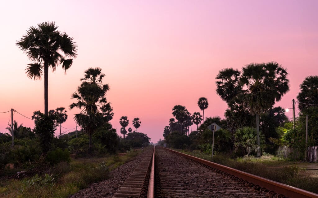 Lange, rechte spoorlijn verdwijnt aan de horizon tussen palmbomen bij schemering in Sri Lanka.