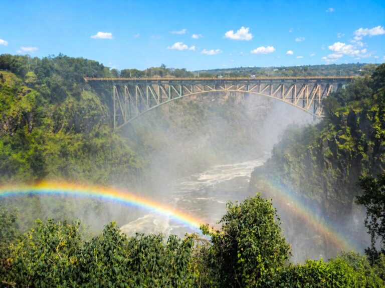 Victoria Falls Bridge over de Batoka-kloof met een dubbele regenboog in de opstijgende nevel van de waterval, groene begroeiing langs de rotswanden