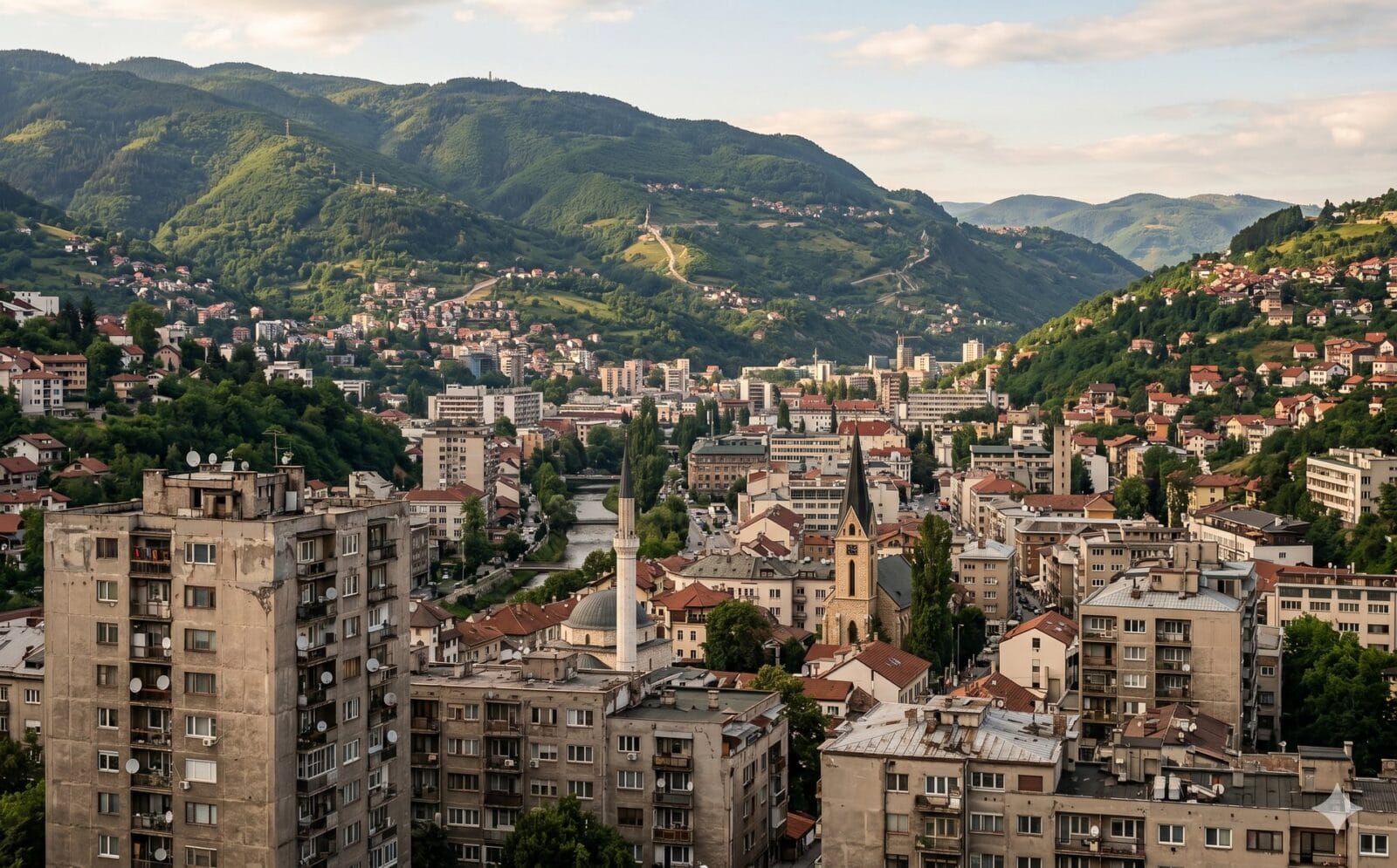 Sarajevo in een smalle vallei tussen steile groene heuvels, met brutalistische betonnen woonblokken, een minaret en een kerktoren