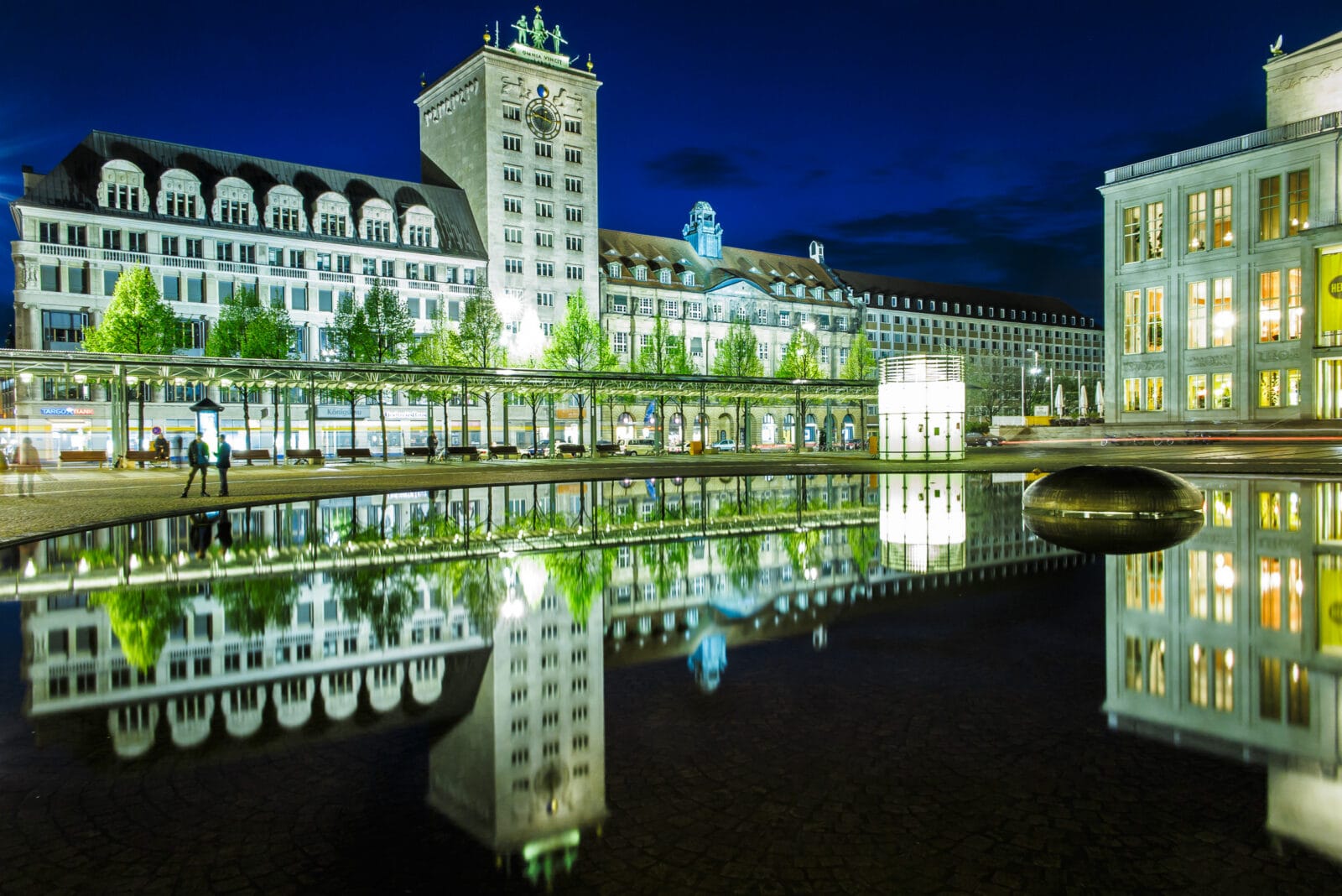 Verlichte gevels weerspiegeld in het waterbassin op de Augustusplatz bij nacht, Leipzig