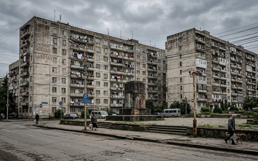 Verweerde Sovjet-betonflats en een leeg standbeeldvoetstuk in een Georgische provinciestad onder een grauwe hemel