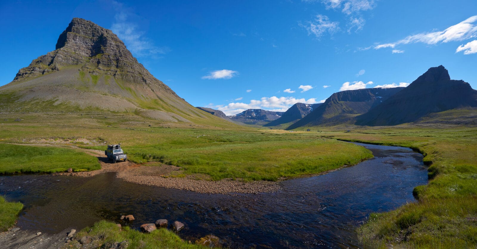 Defender bij een riviertje in een groen dal aan de Svalvogar-weg, Dýrafjörður