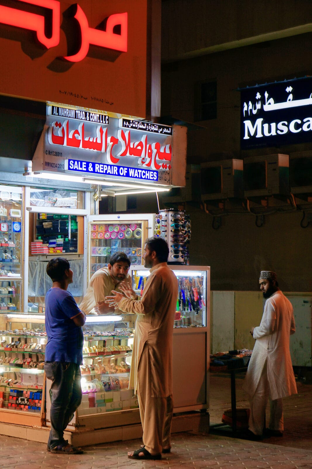 Gesprek bij een horlogewinkel onder neonlicht in Seeb
