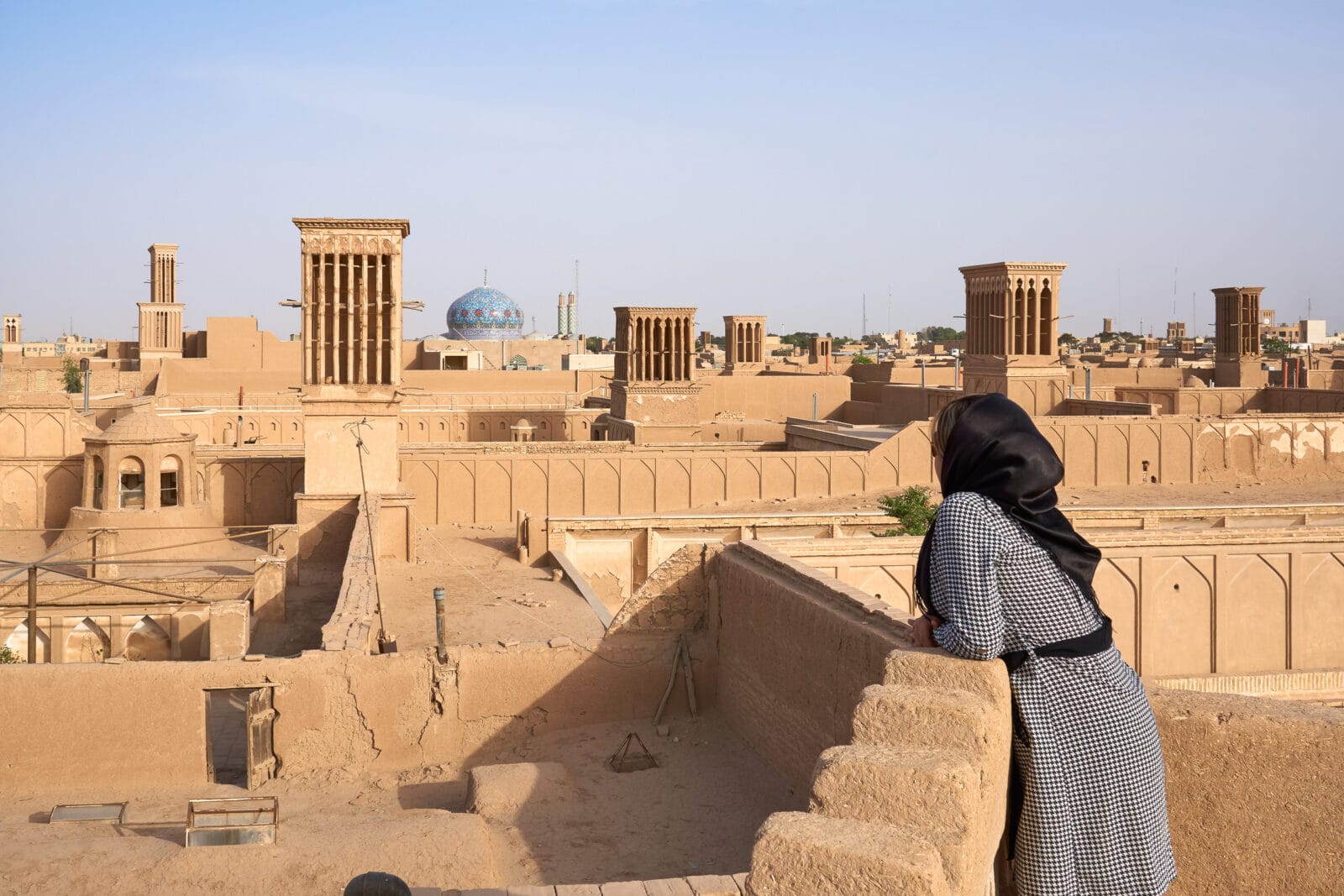 Vrouw kijkt uit over de lemen daken van Yazd