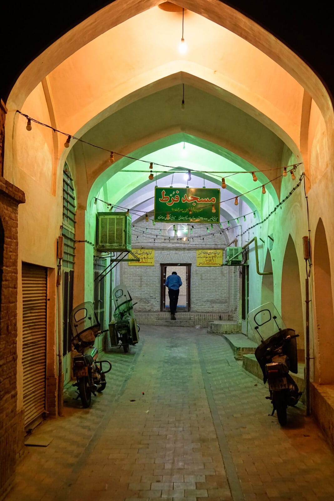 Man loopt de Jameh-moskee van Yazd binnen onder gekleurd licht