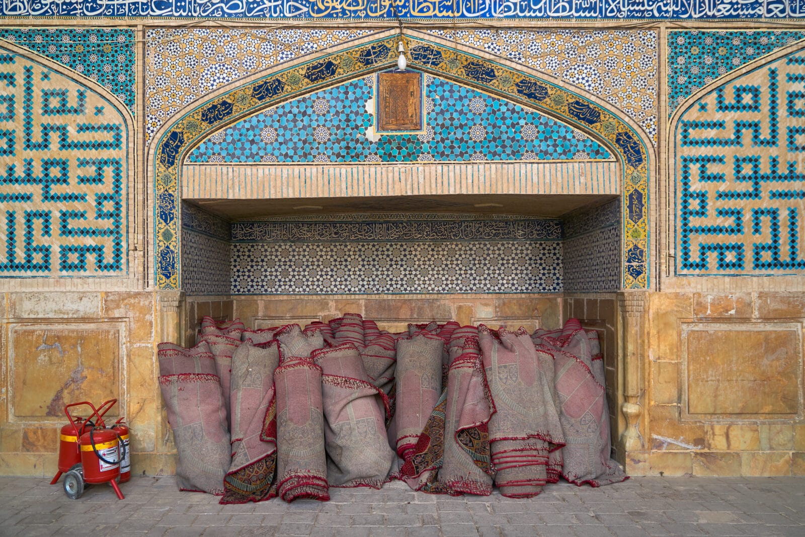 Opgerolde tapijten tegen een betegelde wand in Isfahan