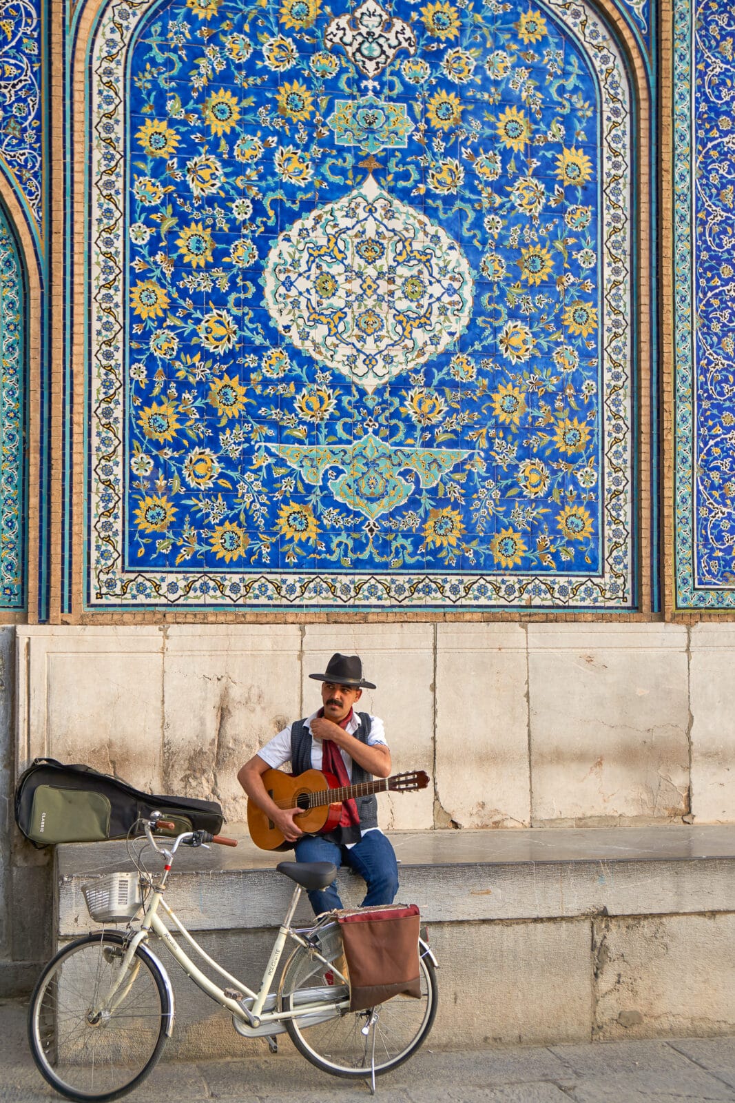 Muzikant pauzeert bij een blauwbetegelde muur in Isfahan