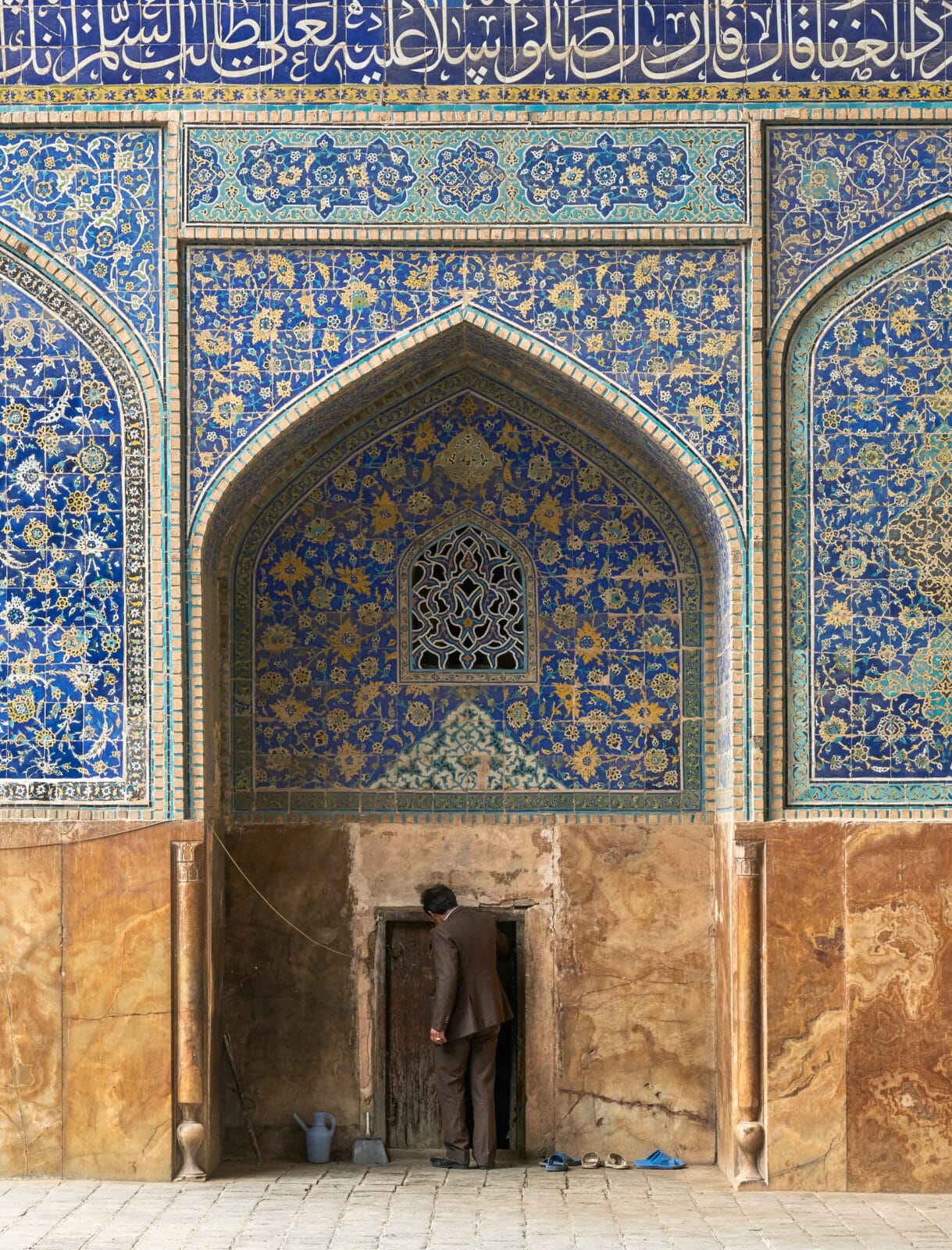Man gaat een deur onder blauw tegelwerk binnen in Isfahan