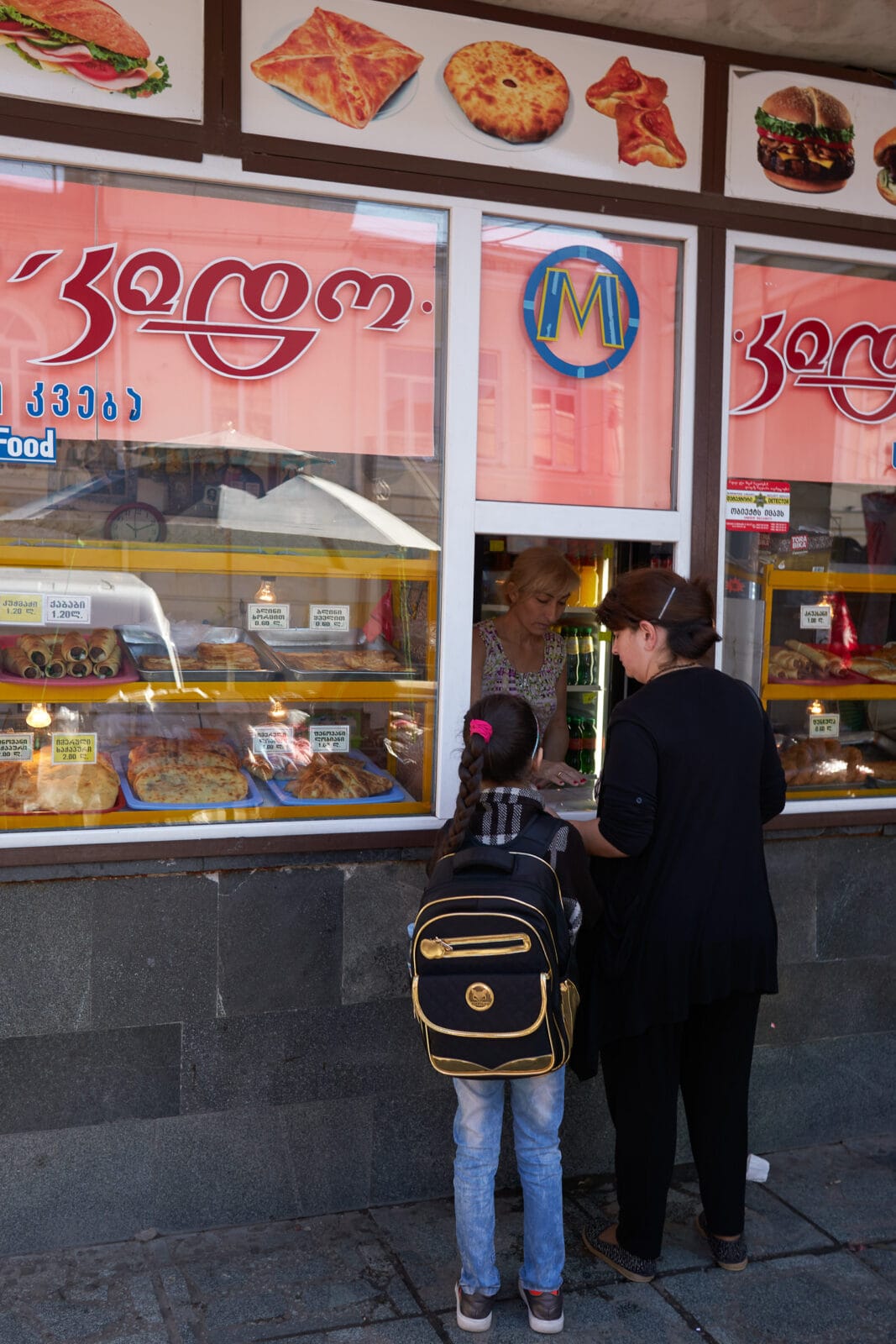 Kind met rugzak koopt eten op straat in Koetaisi