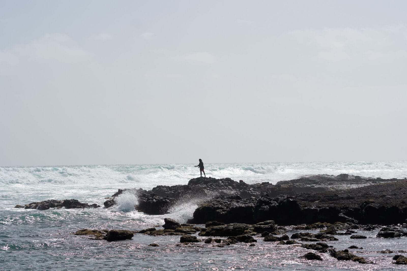Man voor de brekende golven aan de kust van Sal