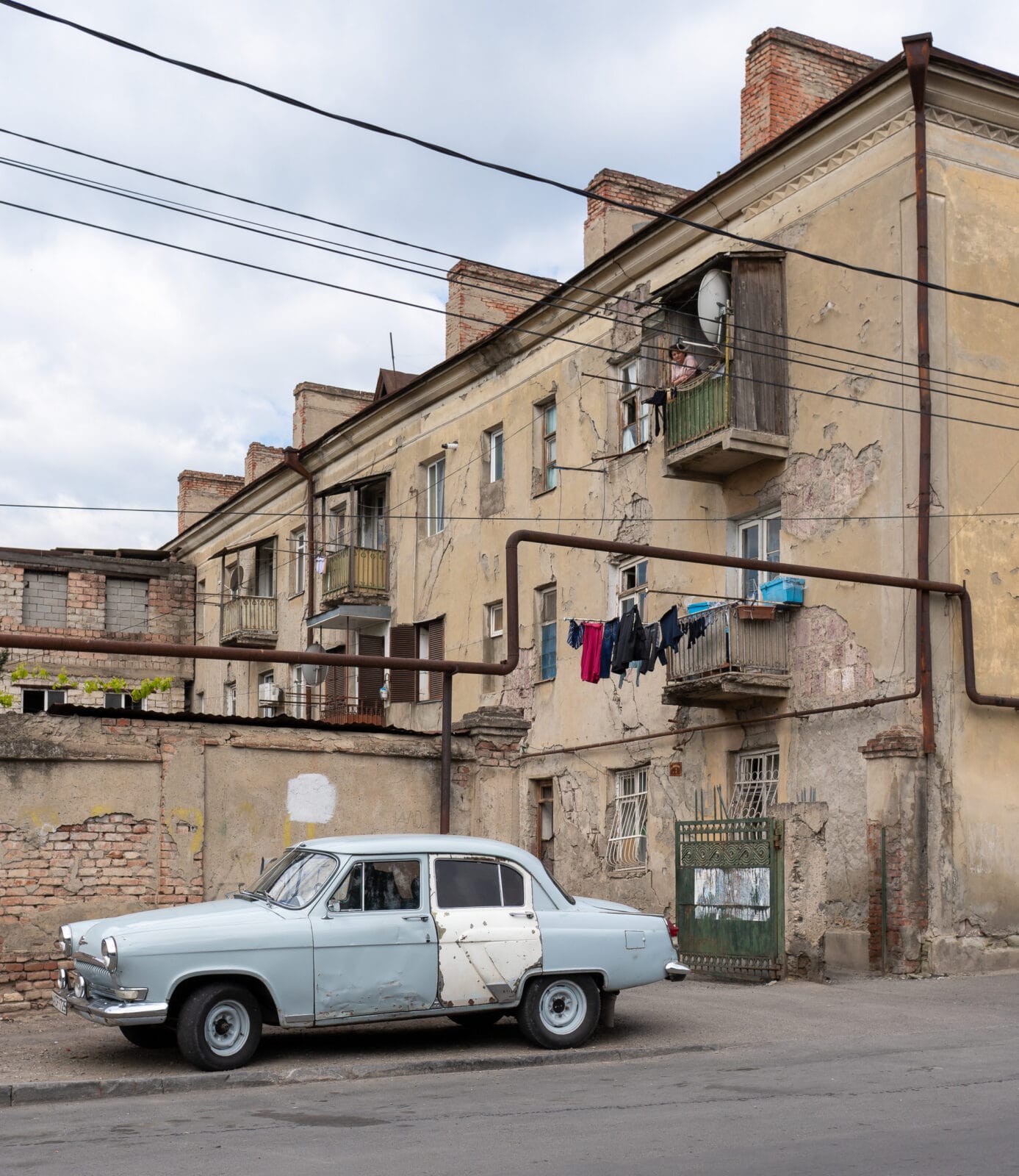 Oude auto voor een verweerd flatgebouw in Tbilisi