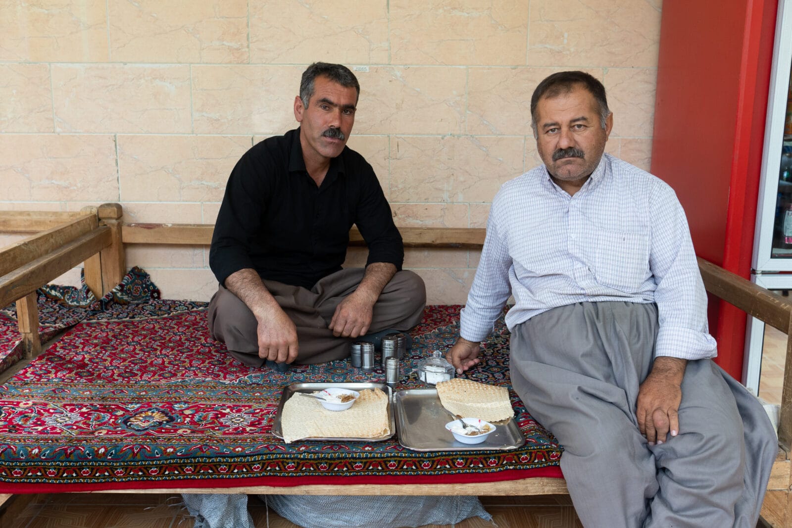 Twee mannen delen een maaltijd op een kleed bij Marivan
