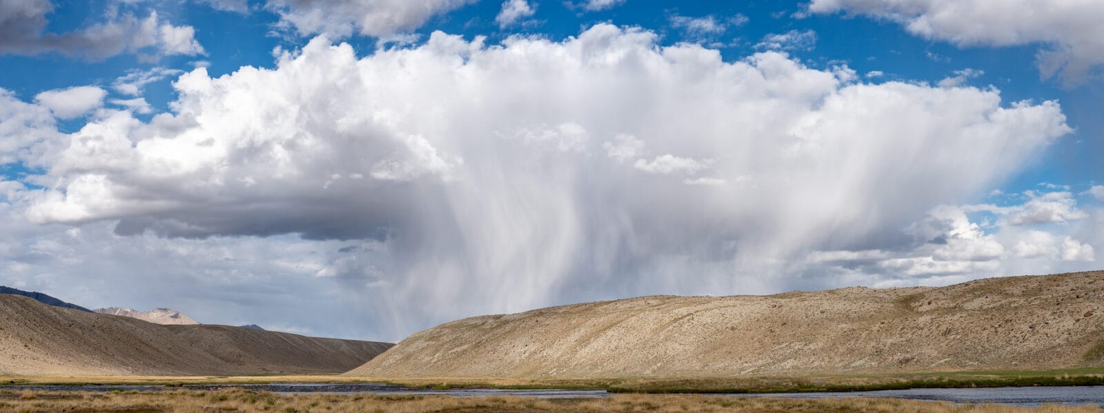 Panorama van regenslierten boven de kale heuvels van de Pamir-hoogvlakte