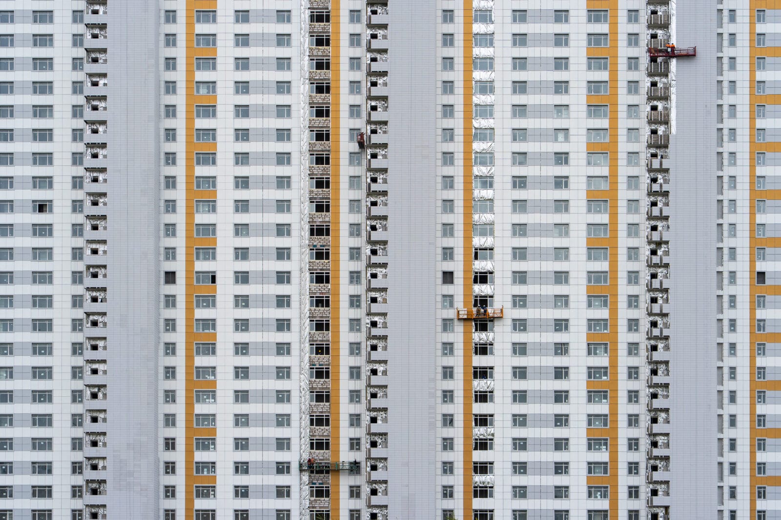 Werklieden op een hangsteiger aan een torenflat in aanbouw in Astana
