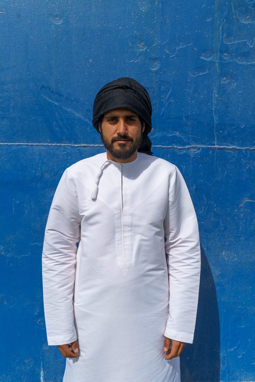 Man in witte dishdasha tegen een blauwe muur in Shannah