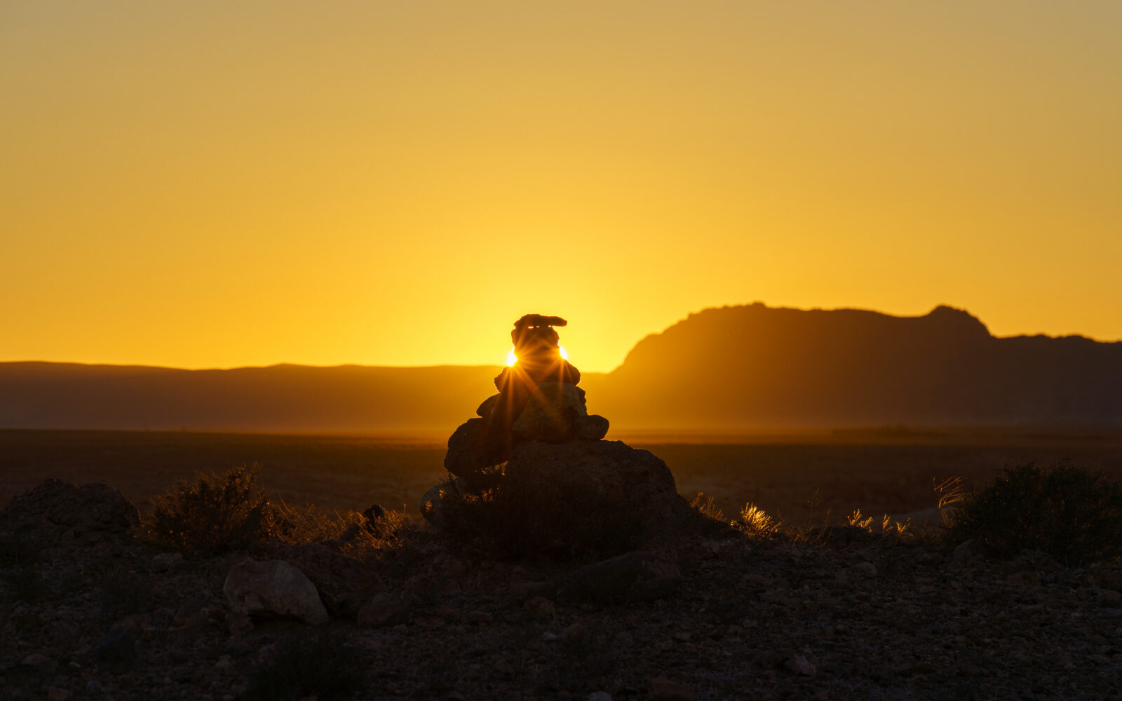 Sunset illuminates cairn in the desert landscape