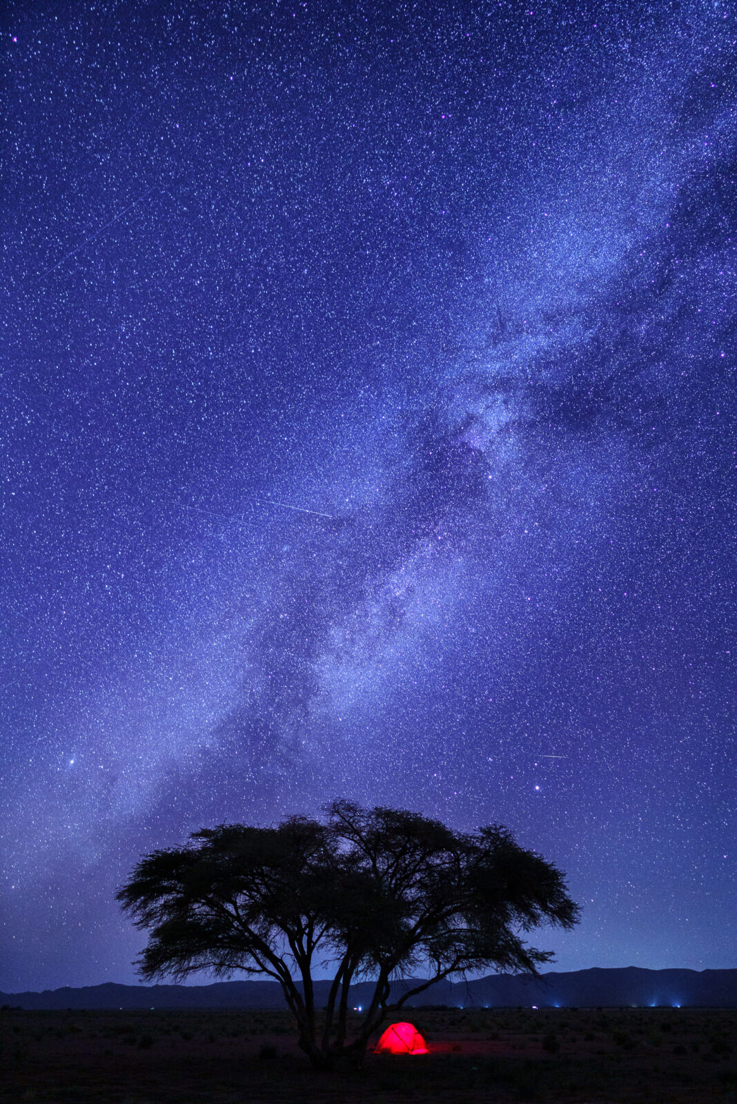 Red tent glows under a starry desert sky