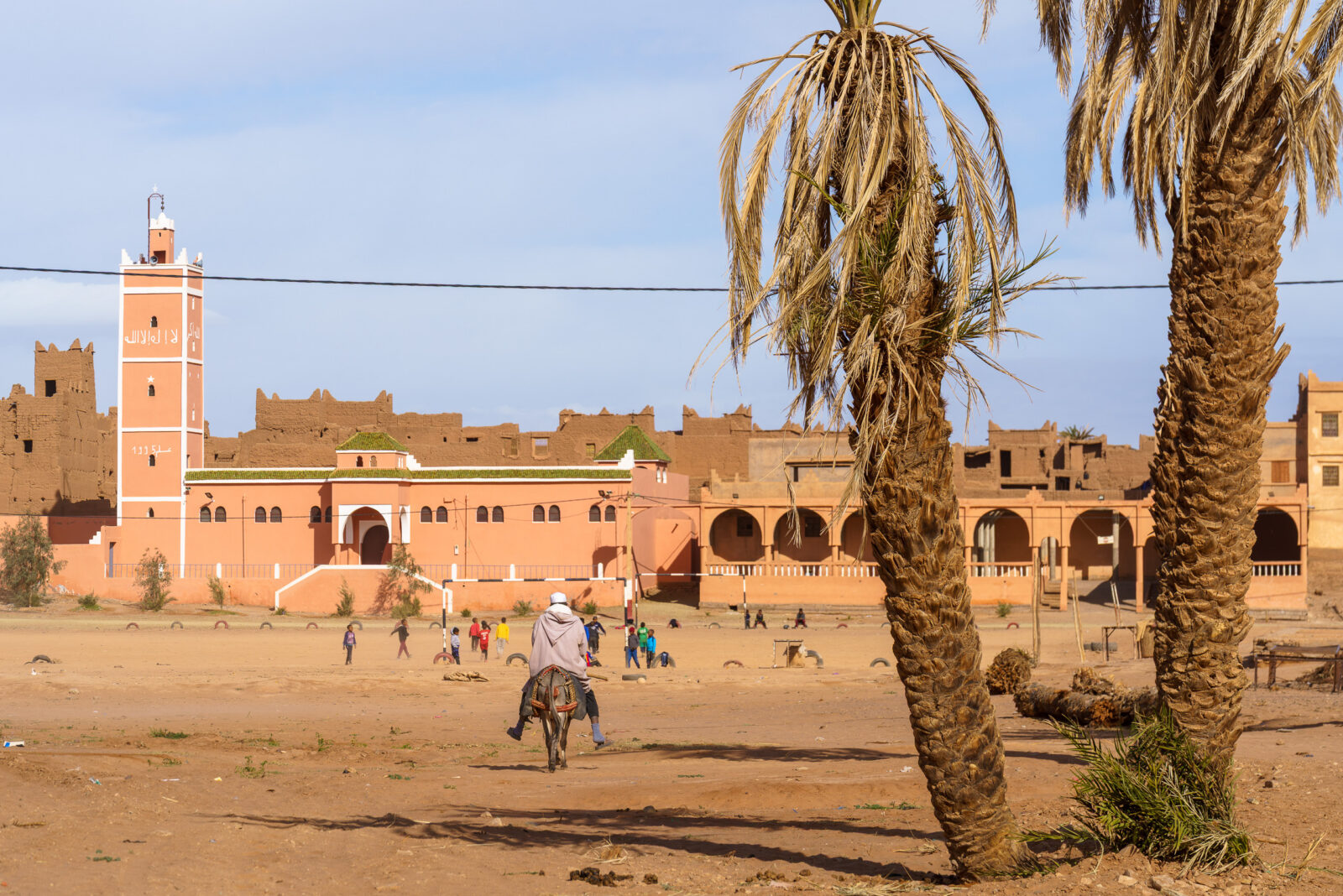A man rides a donkey past a mosque