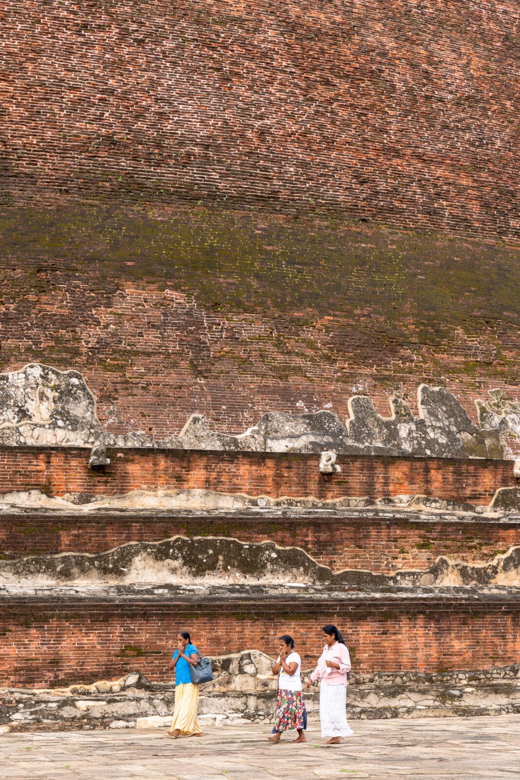 Vrouwen langs een bemoste bakstenen muur in Anuradhapura
