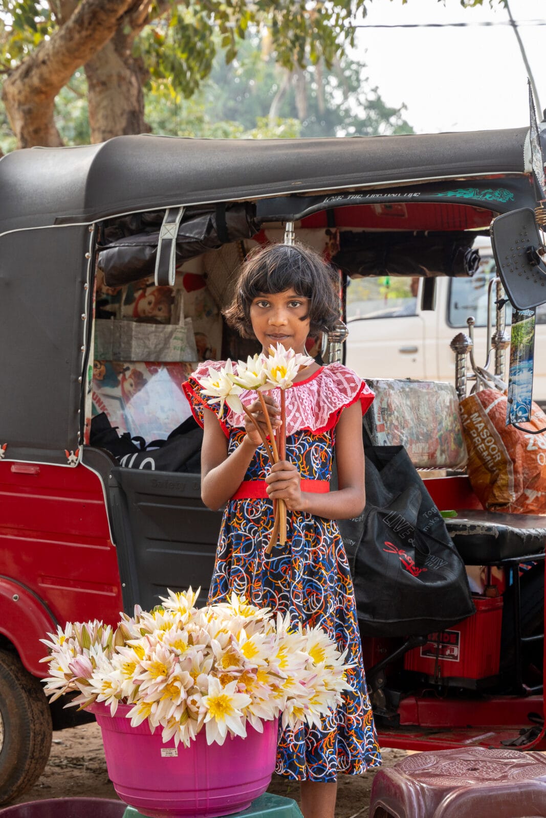 Meisje met lotusbloemen naast een tuktuk in Anuradhapura