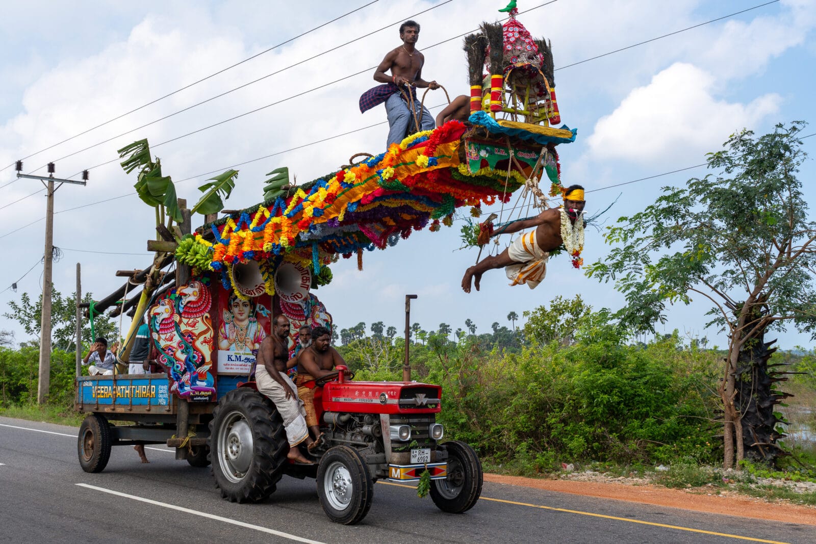 Man hangend aan een versierde wagen tijdens een hindoeprocessie bij Jaffna