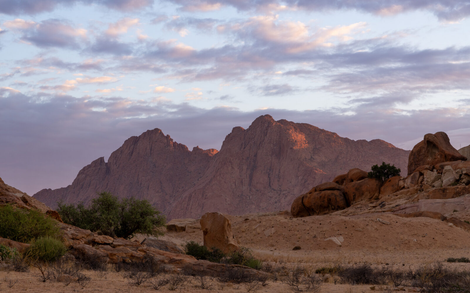 Pastel clouds over sunlit desert mountains