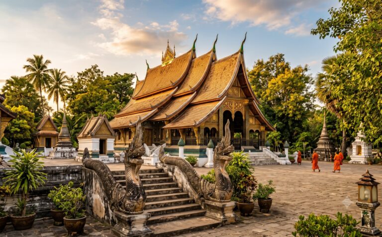 Statige Laotiaanse tempel met meerlaags goudbruin dak en stenen naga-figuren in avondlicht, omringd door tropische bomen