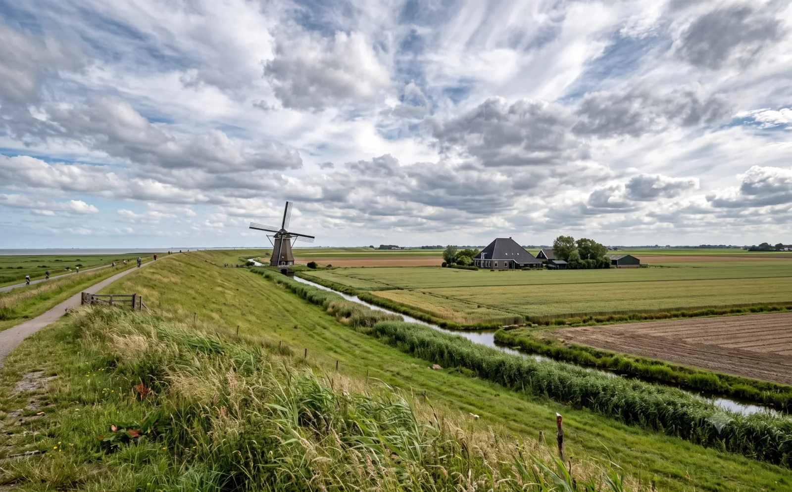 Open polderlandschap met dijk, molen en stolpboerderij onder brede wolkenlucht in de Kop van Noord-Holland