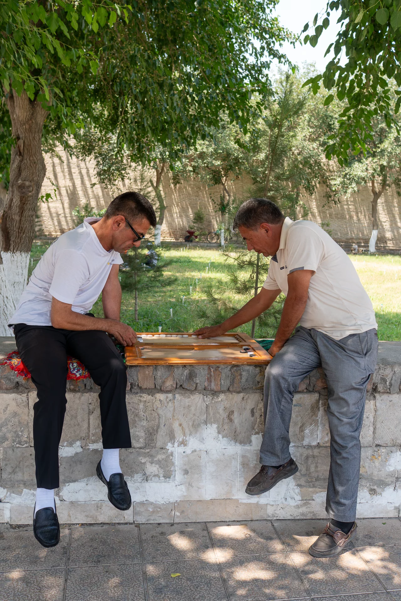 Twee mannen spelen backgammon op een muurtje bij de lemen wal van de Ark in Buchara