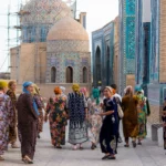 Groep vrouwen in gebloemde jurken tussen de betegelde koepels van Shah-i-Zinda