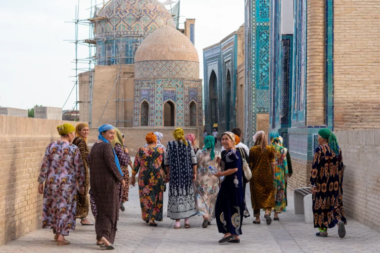 Groep vrouwen in gebloemde jurken tussen de betegelde koepels van Shah-i-Zinda