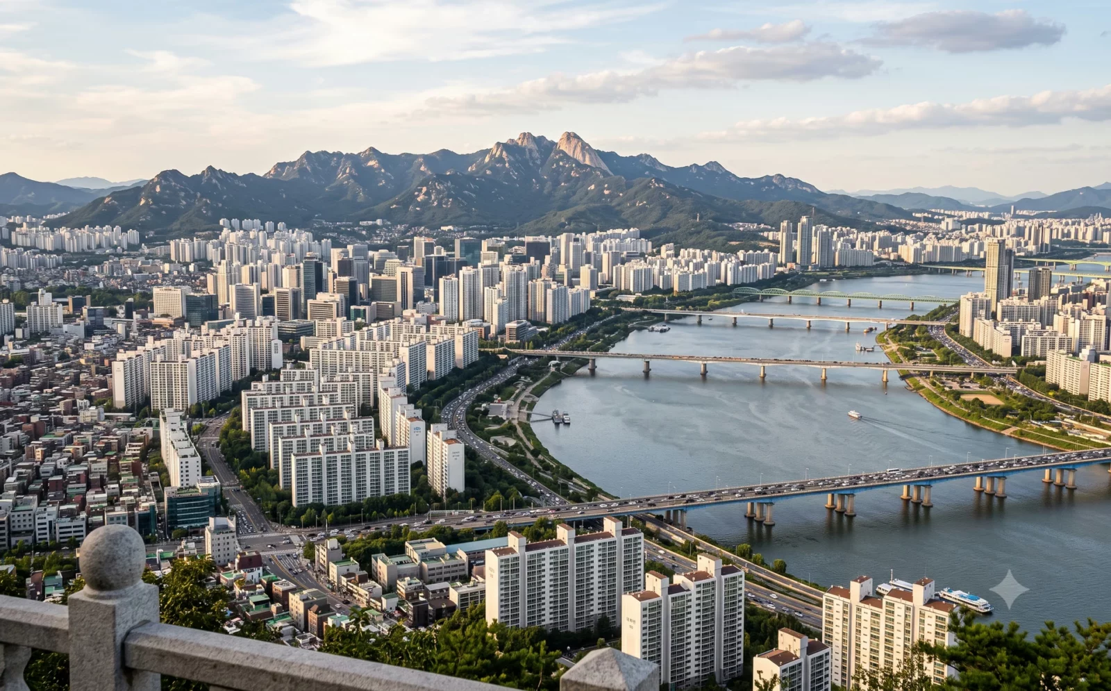 Uitzicht over Seoul vanaf een hoog punt: de brede Han-rivier met bruggen, witte woontorens aan beide oevers en bergen erachter.