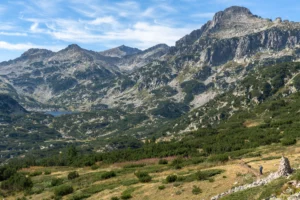 Wandelaar bij een steenmannetje op een pad in het Pirin, met bergdennen, een meer in de diepte en granieten toppen erachter