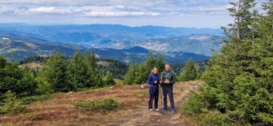 Twee wandelaars met stokken op een open bergrug bij de hut Perelik, met uitzicht over de beboste Rodopen bij Smoljan